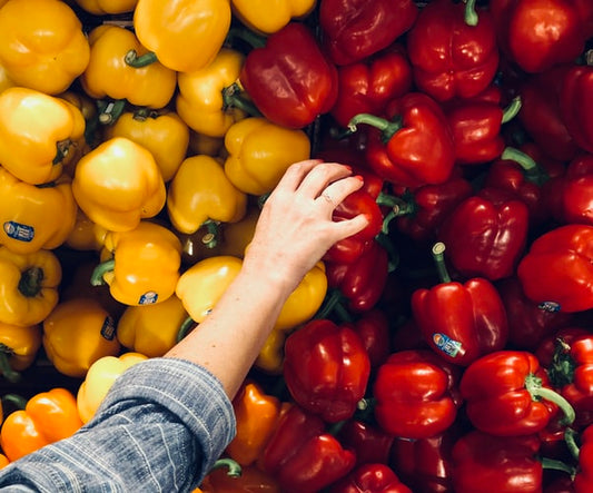Red and yellow bell peppers at a store being picked by a hand